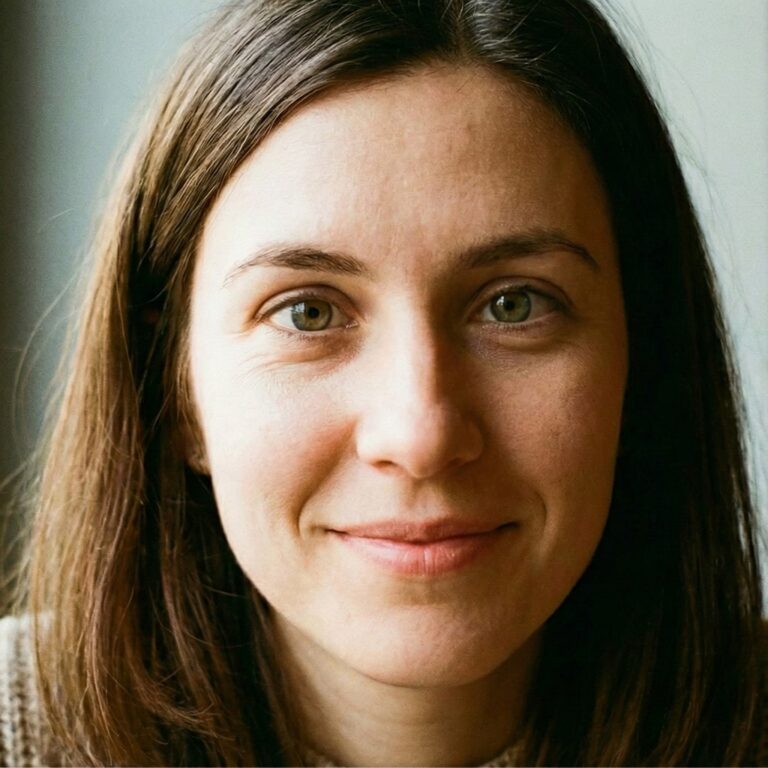 لقطة مقربة لوجه امرأة شابة ذات شعر بني وعينين خضراوين فاتحتين. تعبر عن التفاؤل والود، مع خلفية ضبابية ناعمة وإضاءة طبيعية هادئة.